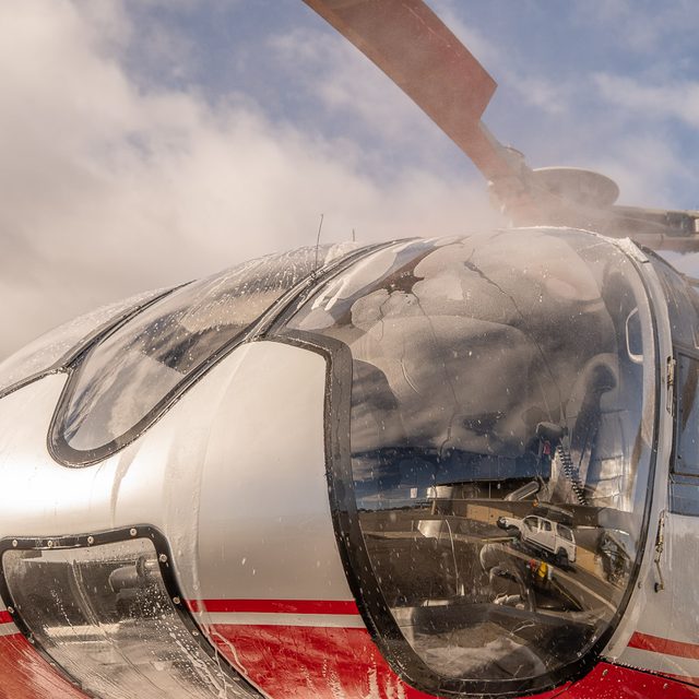 Detailer washing the cockpit glass of a helicopter under a cloudy sky