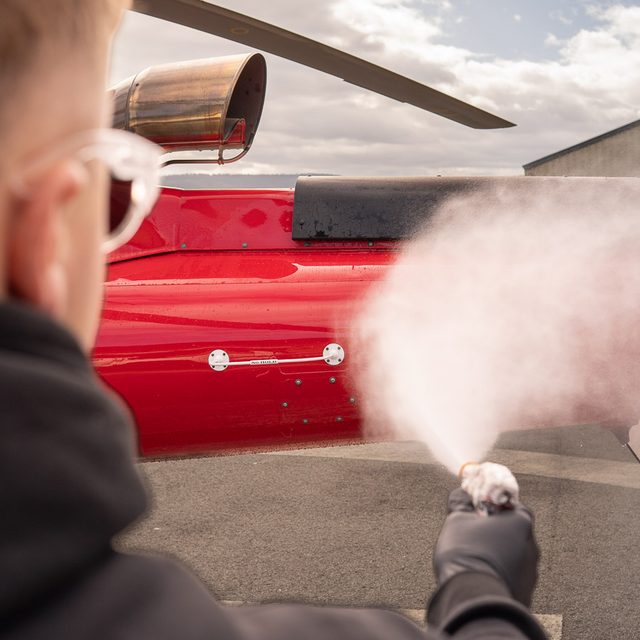 Over-the-shoulder shot of a detailer rinsing a helicopter fuselage